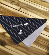 Load image into Gallery viewer, A triangular pet bandana with a black and navy blue striped pattern, featuring the white text 'Free Hugs' and a paw print logo, laid flat on a wooden plank surface.