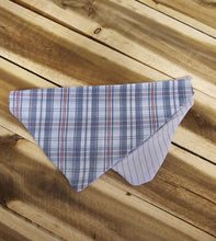 Load image into Gallery viewer, A triangular bandana-style pet collar or scarf made of plaid fabric, shown laid flat on a wooden plank surface. The front side has a blue, white, and red plaid pattern, and the reverse side is light lavender with thin dark stripes.