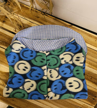 Load image into Gallery viewer, A fleece pet coat with a blue, green, and white smiley face pattern on the outside and a light blue and white gingham pattern on the inside, displayed on a wooden surface.
