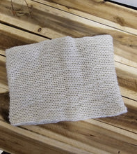 Load image into Gallery viewer, A cream handmade knitted neck warmer, laid flat on a rustic wooden plank surface.