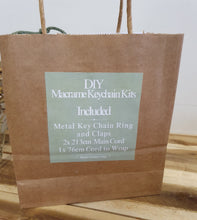 Load image into Gallery viewer, Brown paper bag with a label for DIY Macrame Keychain Kits on a wooden surface.