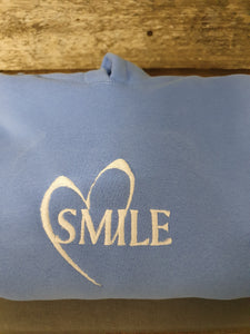 Blue jumper with white embrodiered white text "Smile" with a heart