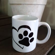 Load image into Gallery viewer, White mug with black heart and paw design on a wood background
