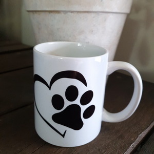 White mug with black heart and paw design on a wood background