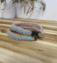 Load image into Gallery viewer, Two braided dog collars, one pink and one blue, hanging on a wooden surface with a blurred natural background.
