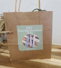 Load image into Gallery viewer, Brown paper bag with a label for DIY Macrame Keychain Kits on a wooden surface.

