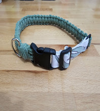 Load image into Gallery viewer, A handmade dog collar made of sage green Cotton with a black plastic quick-release buckle and a white patterned fabric lining, resting on a light wood surface.
