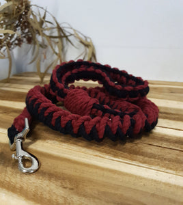 Red and black braided dog leash with a silver clasp on a wooden surface.