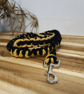 Black and yellow braided dog leash with a silver clasp on a wooden surface.