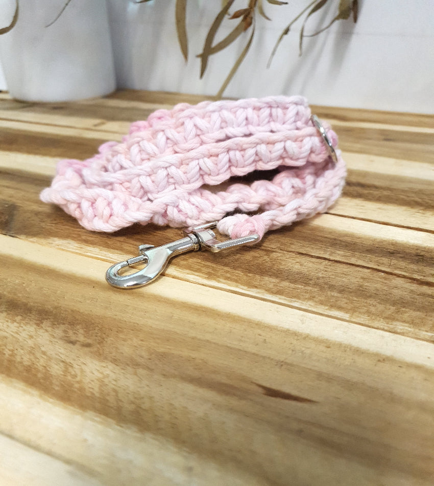 Pink macrame dog leash with a metal clip on a wooden surface