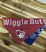 Load image into Gallery viewer, A triangular dog bandana laid flat on a wooden surface. The front panel is red and white gingham with large white text reading 'Wiggle Butt' and a white paw print heart graphic.
