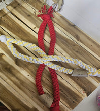 Load image into Gallery viewer, A braided rope dog toy with a thick red section and two braided sections in white and yellow, laid out on a wooden pallet.
