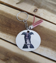 Load image into Gallery viewer, Keychain with circular tag featuring a Grey Hound illustration on a wooden surface

