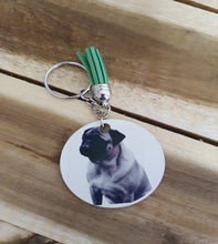 Load image into Gallery viewer, Keychain with a circular tag featuring a pug and a green tassel on a wooden surface
