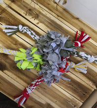 Load image into Gallery viewer, A multi-colored fabric dog chew toy made of gray felt strips with red, white, yellow, and green accents, laid out on a wooden pallet.
