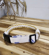Load image into Gallery viewer, A white and Yellow with a blue patterned fabric strap and black plastic buckle, shown on a wooden surface.
